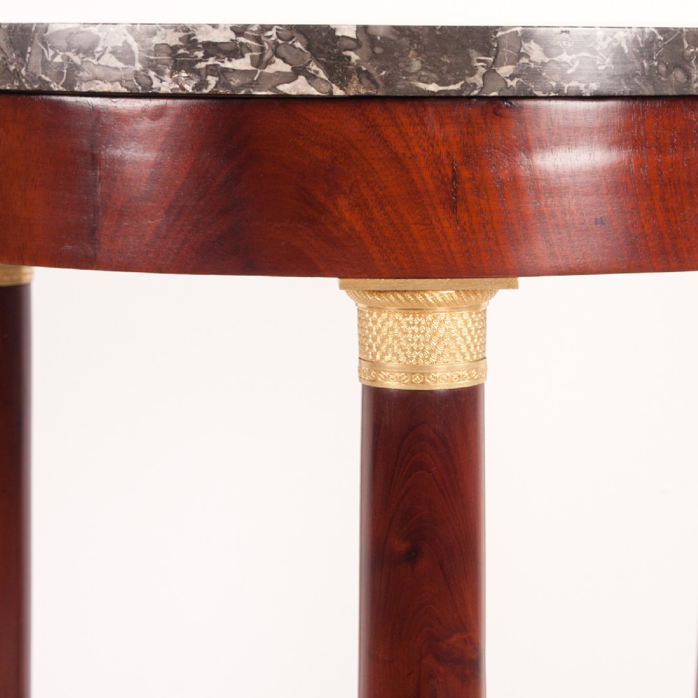 A 19th-century French mahogany gueridon side table with a round grey marble top, three cylindrical legs with gilt mounts, and a tri-form concave base. View VII