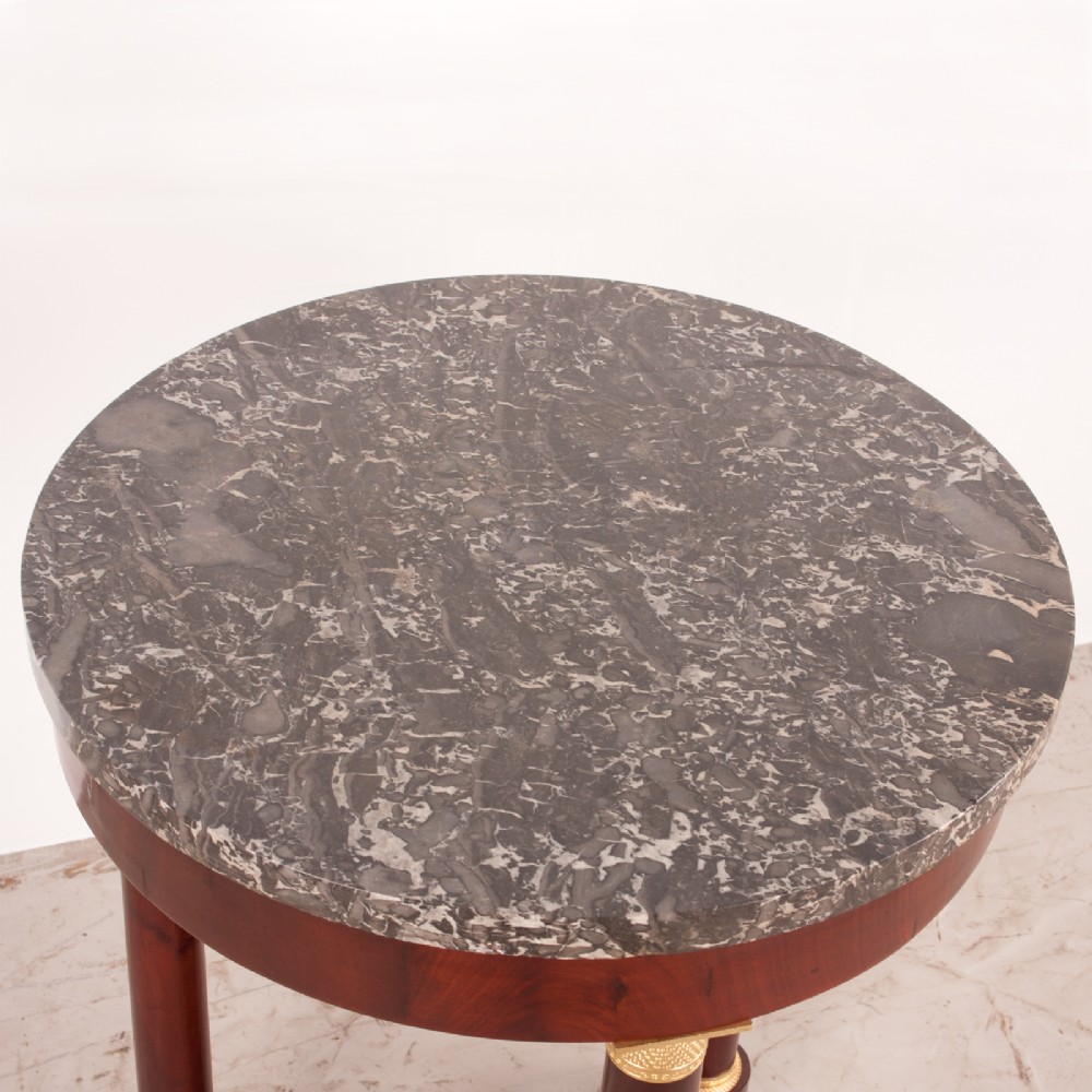 A 19th-century French mahogany gueridon side table with a round grey marble top, three cylindrical legs with gilt mounts, and a tri-form concave base. View VIII