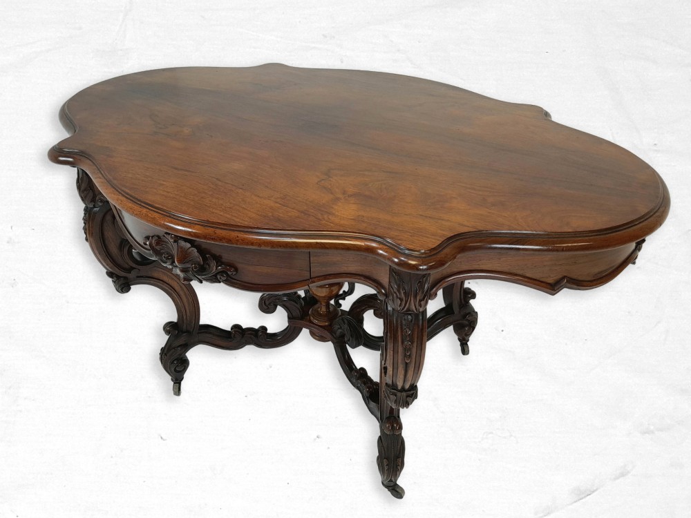 A Victorian rosewood centre table featuring a serpentine shaped top, intricate carved frieze, scroll legs, and brass castors.