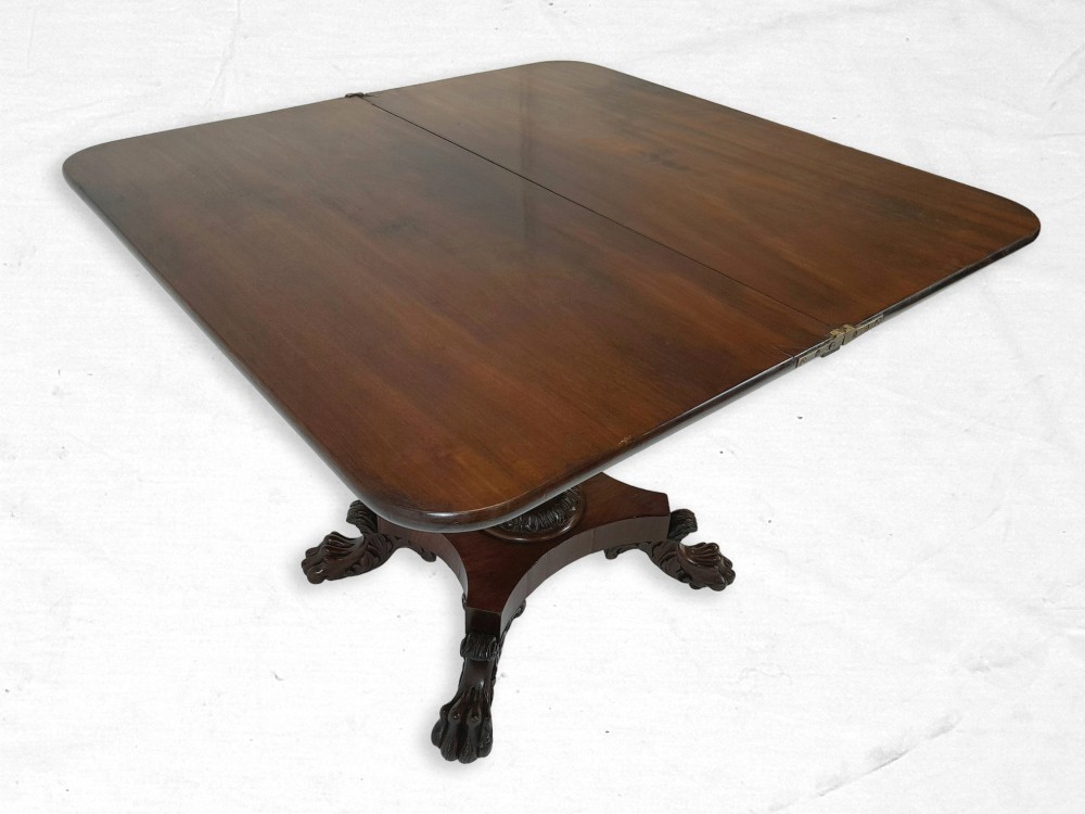 A William IV polished mahogany fold-over tea table featuring a swivel top on a carved central pedestal base with lion paw feet.