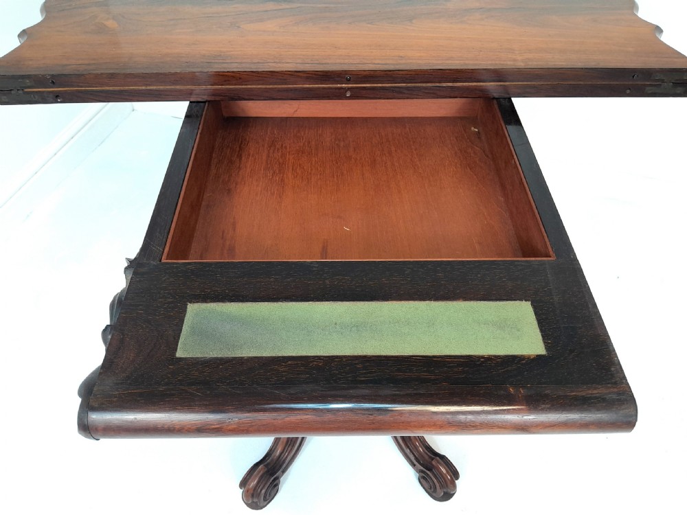 An antique Victorian rosewood card table featuring a serpentine shaped top, carved scroll frieze, central turned pedestal, and a carved quadform base. View VIII