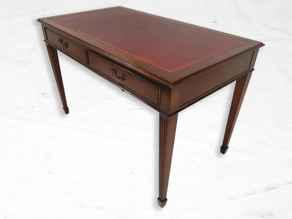 A mahogany writing table featuring a burgundy leather inset top, two frieze drawers with brass handles, and reeded square tapered legs.