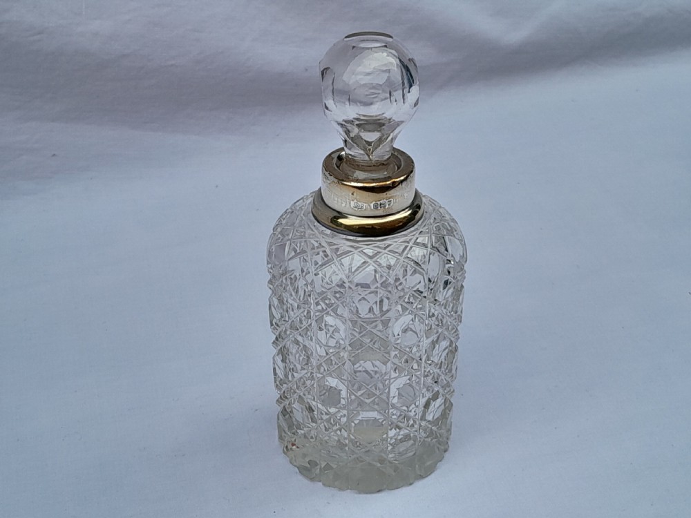 A cylindrical cut glass scent bottle featuring a hallmarked sterling silver collar and a faceted round glass stopper.