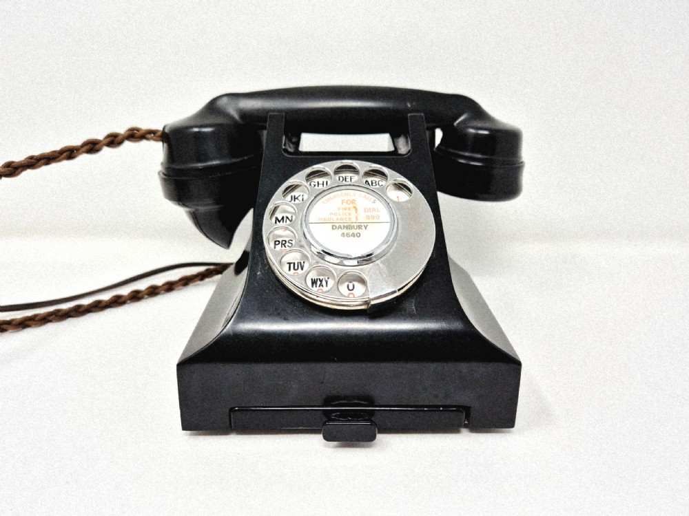 A black Bakelite rotary telephone featuring a chrome dial face, pull-out directory tray, and a braided textile cord.