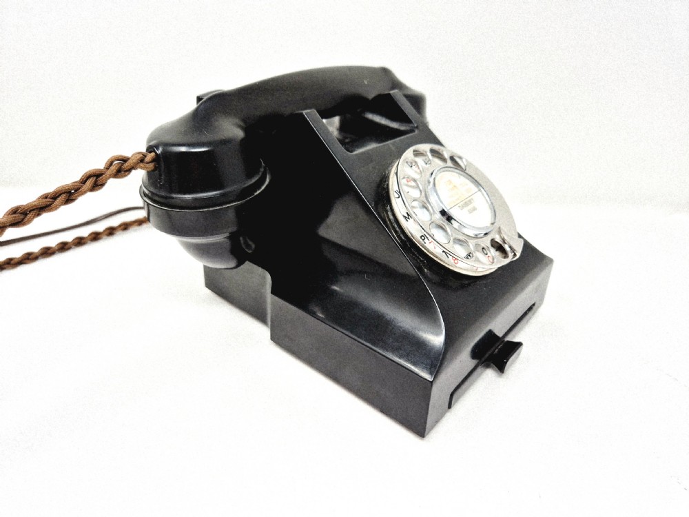 A black Bakelite rotary telephone featuring a chrome dial face, pull-out directory tray, and a braided textile cord. View II