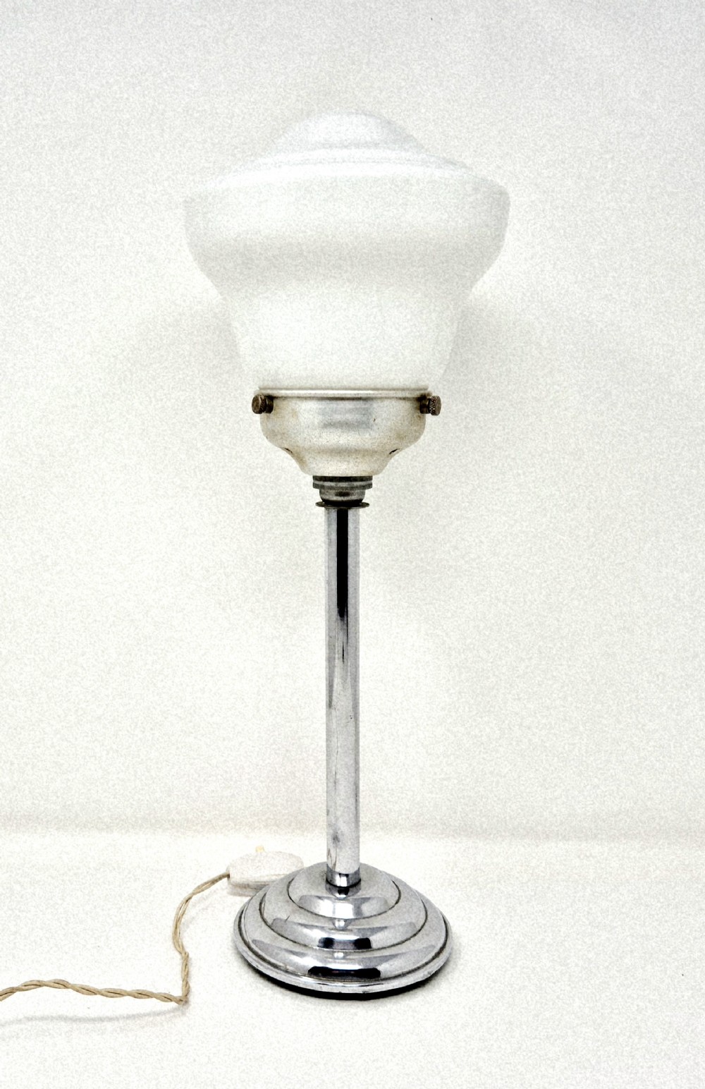 An Art Deco table lamp featuring a stepped polished chrome base, slender vertical column, and a white frosted glass shade.
