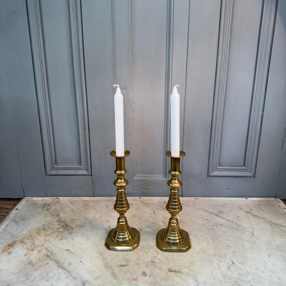A pair of Victorian brass candlesticks featuring turned beehive columns on stepped square bases, displayed with white taper candles.