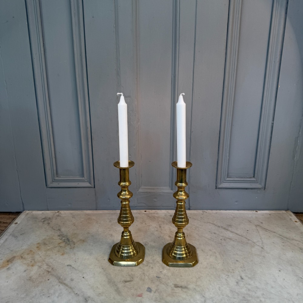 A pair of Victorian brass candlesticks featuring turned beehive columns on stepped square bases, displayed with white taper candles. View II