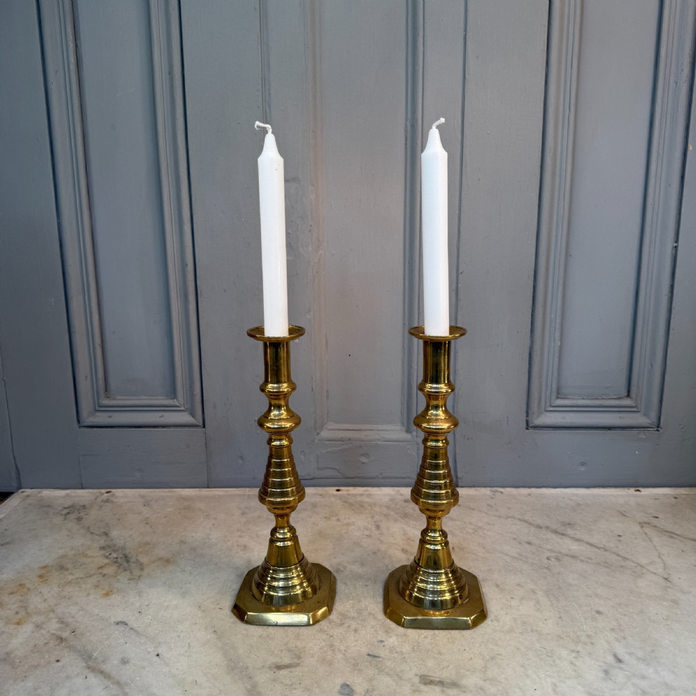 A pair of Victorian brass candlesticks featuring turned beehive columns on stepped square bases, displayed with white taper candles. View III