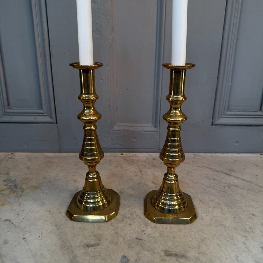 A pair of Victorian brass candlesticks featuring turned beehive columns on stepped square bases, displayed with white taper candles. View IV