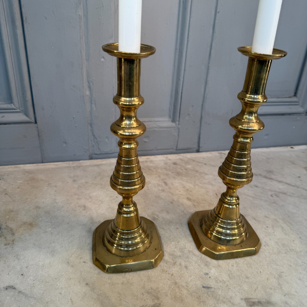 A pair of Victorian brass candlesticks featuring turned beehive columns on stepped square bases, displayed with white taper candles. View V