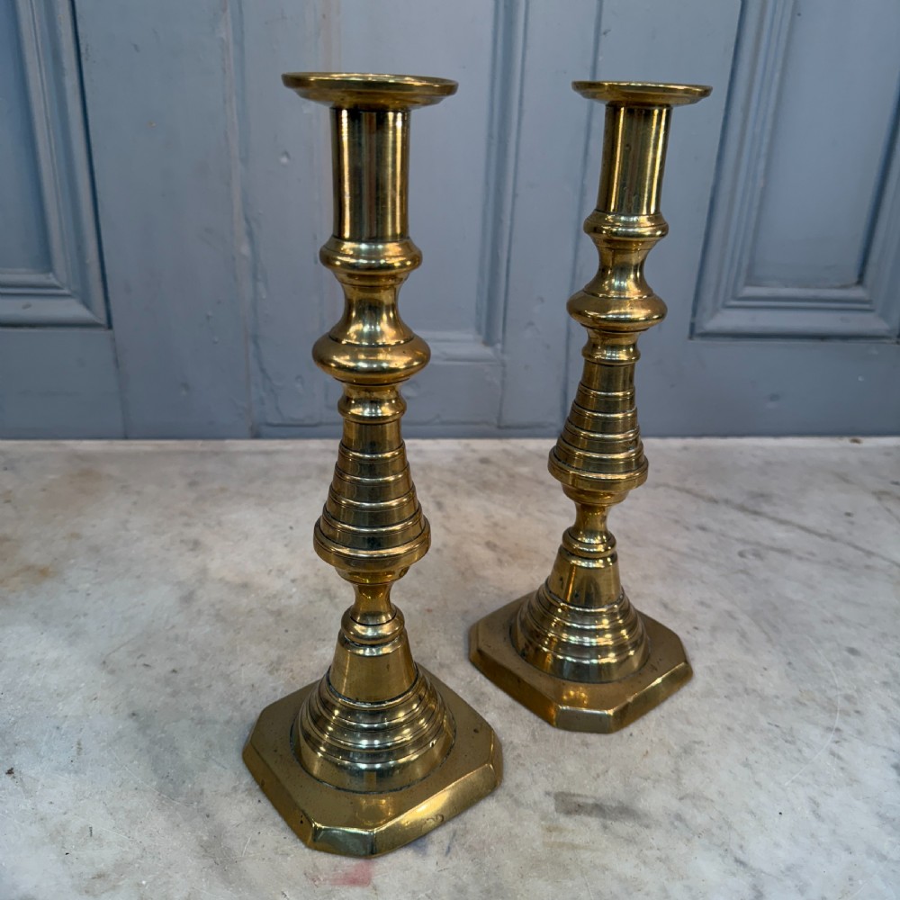 A pair of Victorian brass candlesticks featuring turned beehive columns on stepped square bases, displayed with white taper candles. View VI