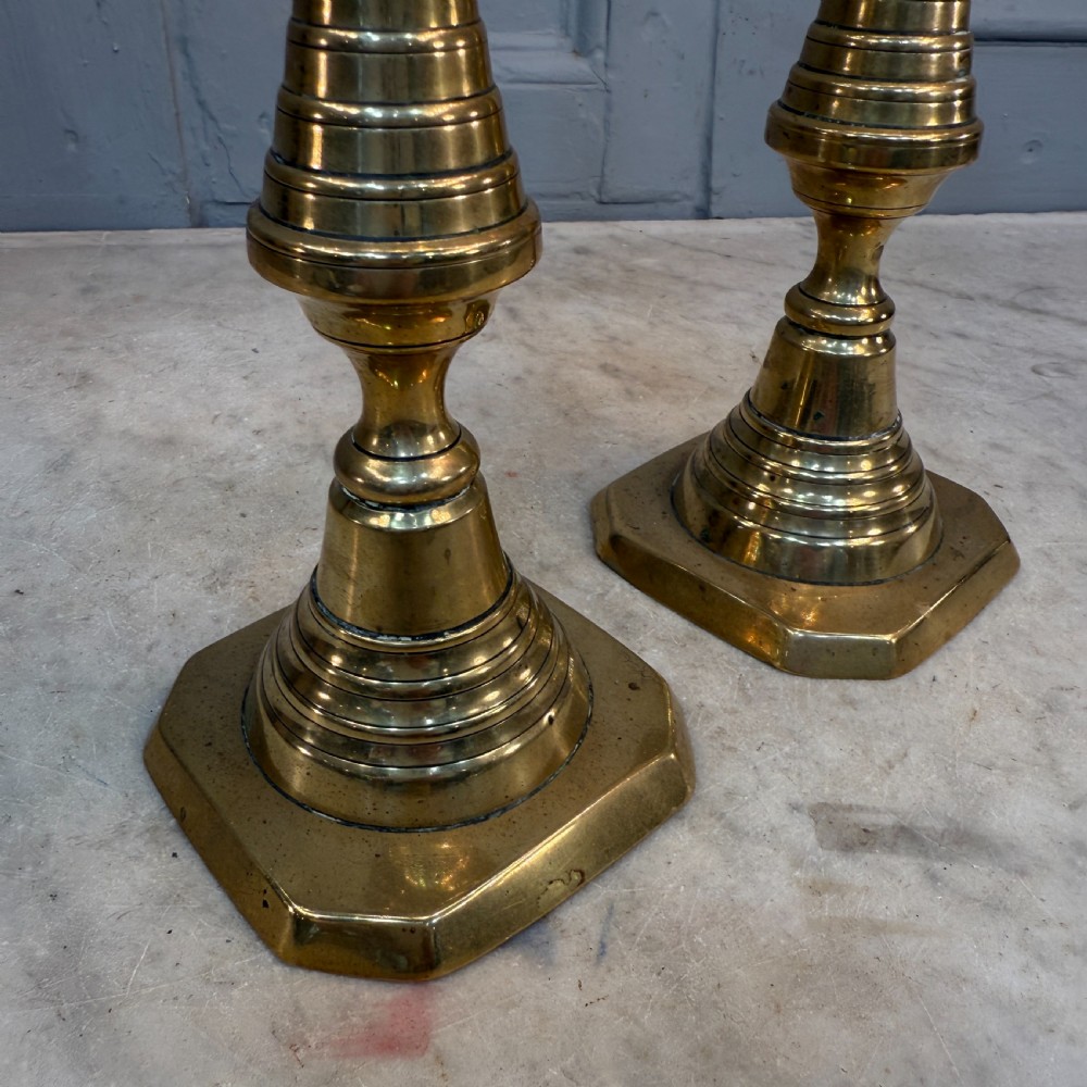 A pair of Victorian brass candlesticks featuring turned beehive columns on stepped square bases, displayed with white taper candles. View VII