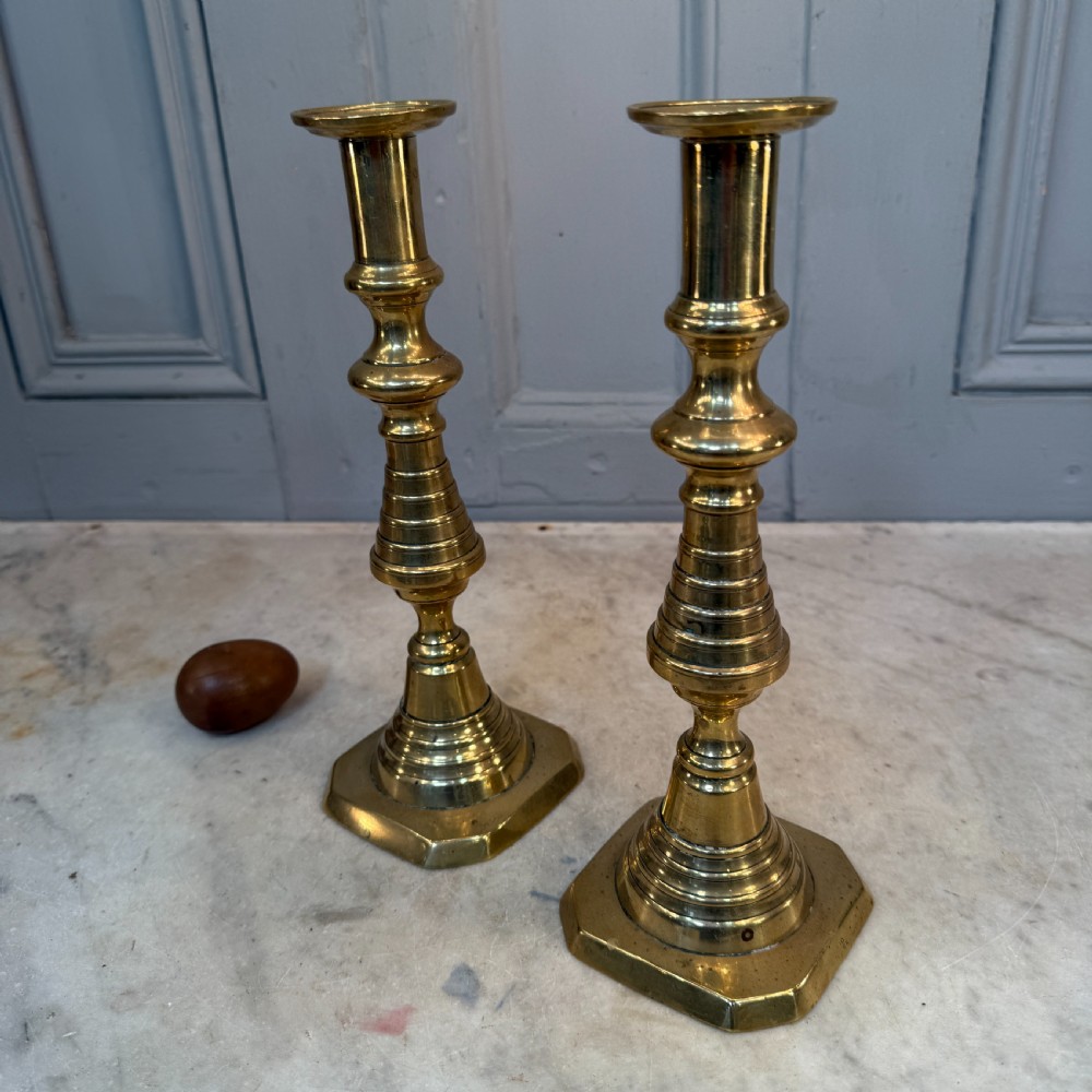 A pair of Victorian brass candlesticks featuring turned beehive columns on stepped square bases, displayed with white taper candles. View IX
