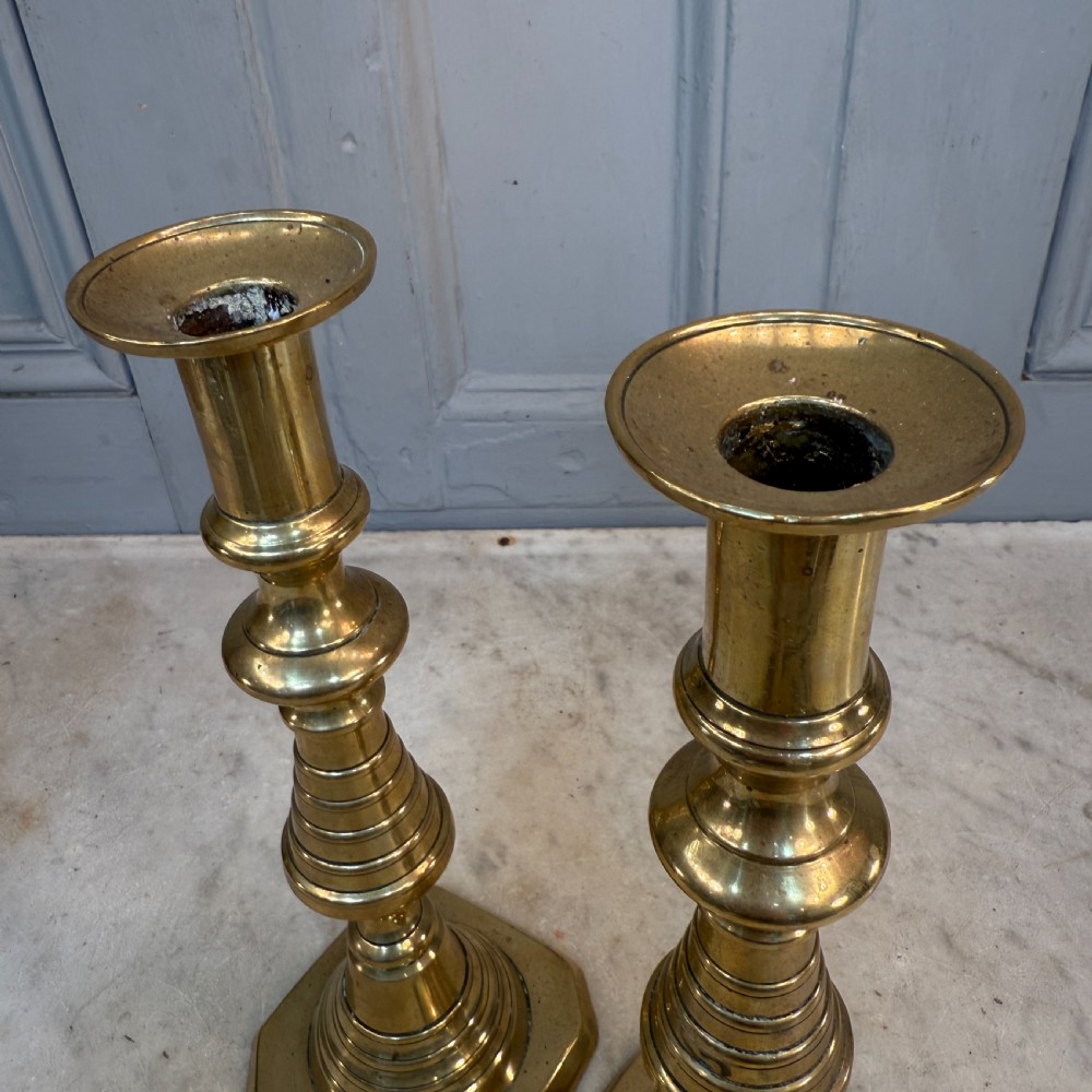 A pair of Victorian brass candlesticks featuring turned beehive columns on stepped square bases, displayed with white taper candles. View X