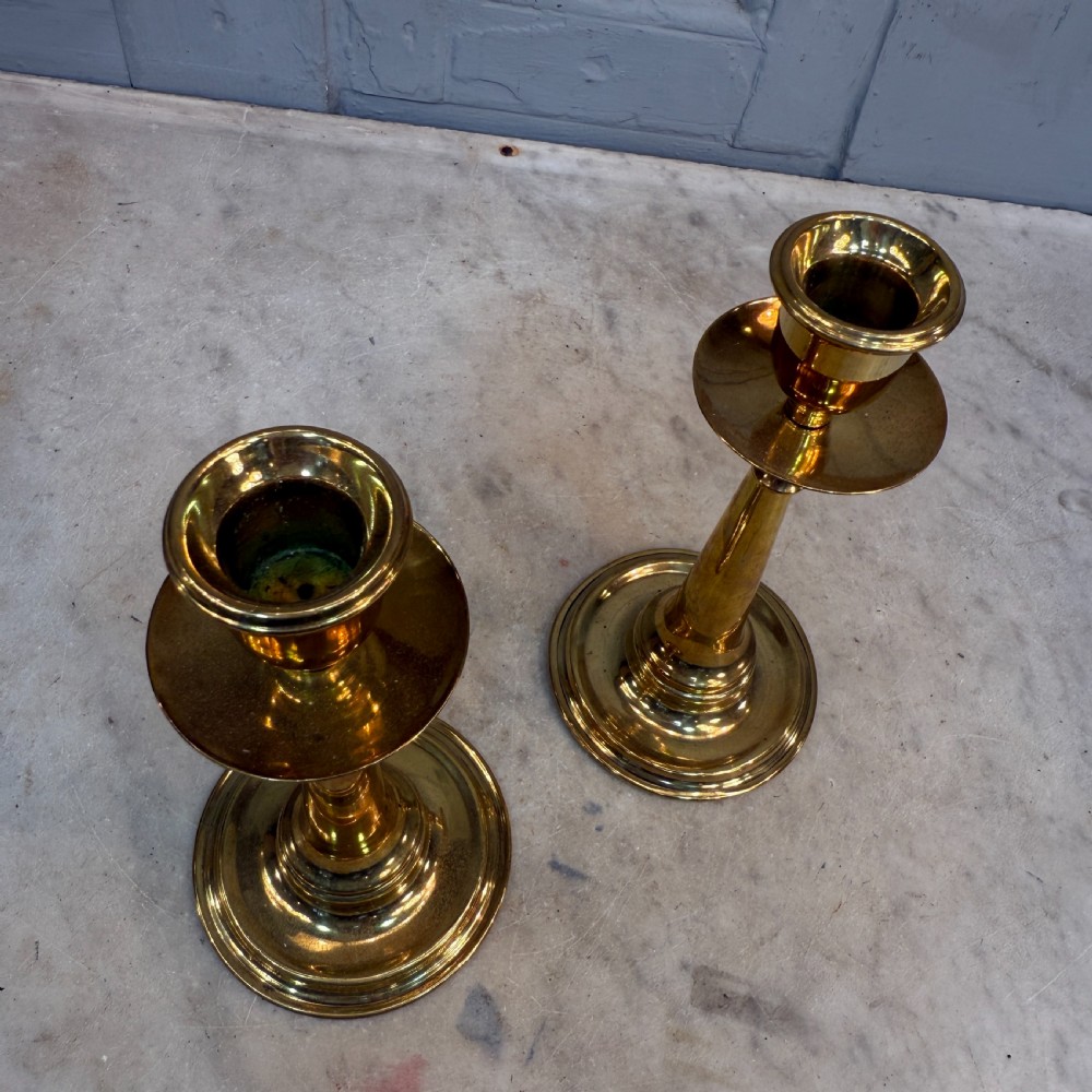 A pair of Arts and Crafts brass candlesticks featuring tapered stems, circular drip pans, and stepped circular bases holding white taper candles. View VII