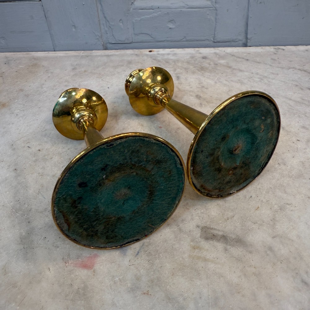 A pair of Arts and Crafts brass candlesticks featuring tapered stems, circular drip pans, and stepped circular bases holding white taper candles. View VIII