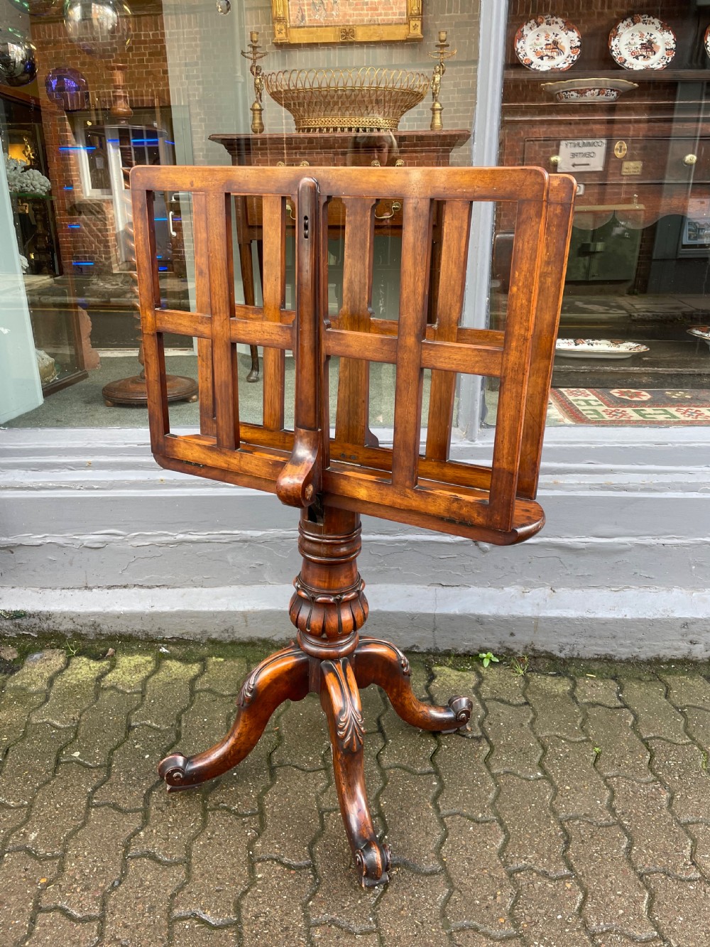 An antique wooden folio stand featuring a slatted double-sided display frame mounted on a carved pillar and tripod base.