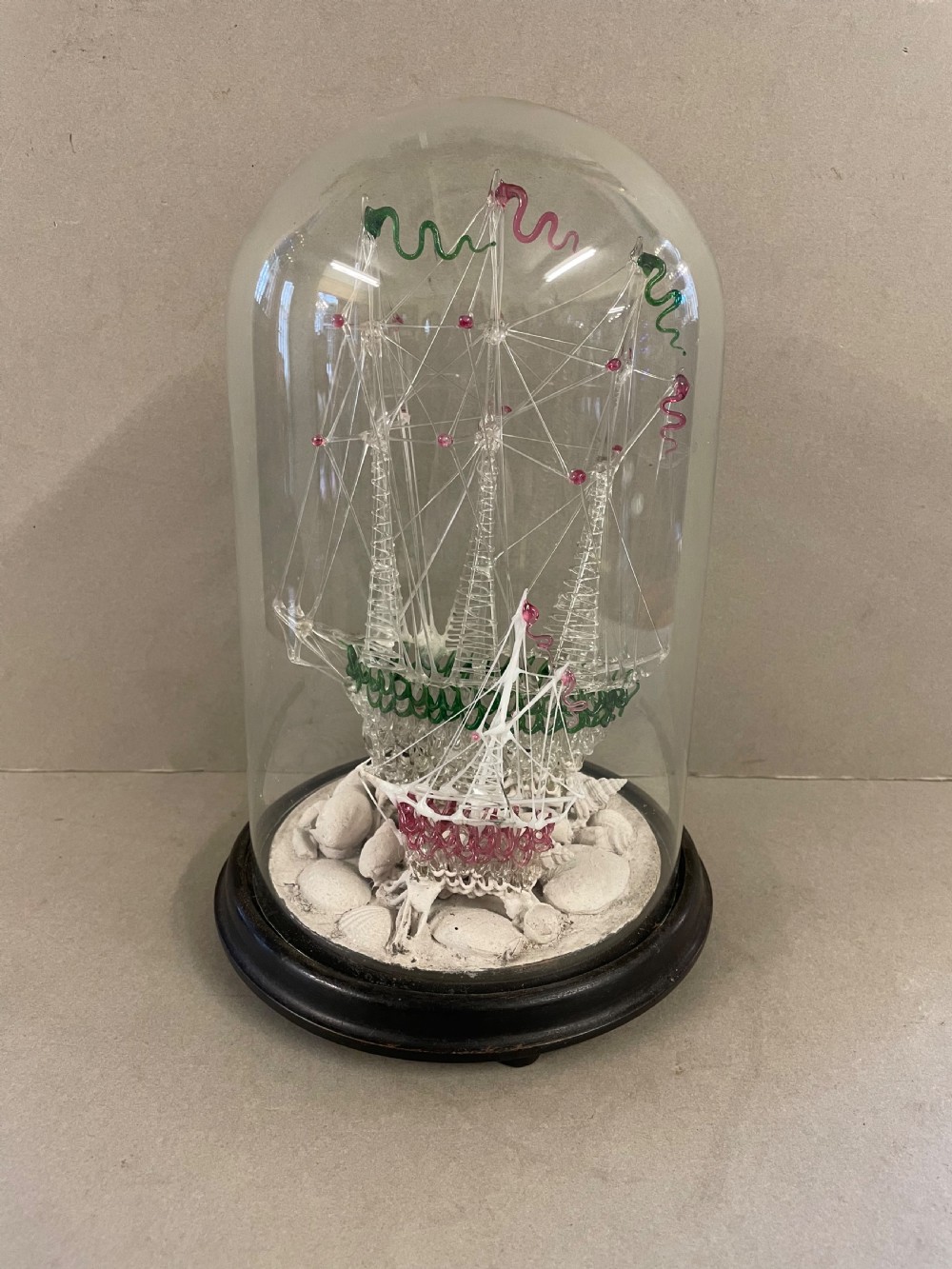 A detailed model of a sailing ship made from spun glass, enclosed inside a glass display dome on a dark wooden base.