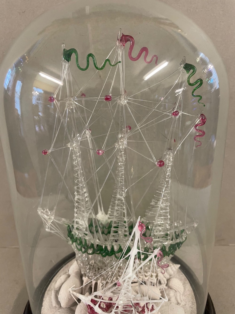 A detailed model of a sailing ship made from spun glass, enclosed inside a glass display dome on a dark wooden base. View II