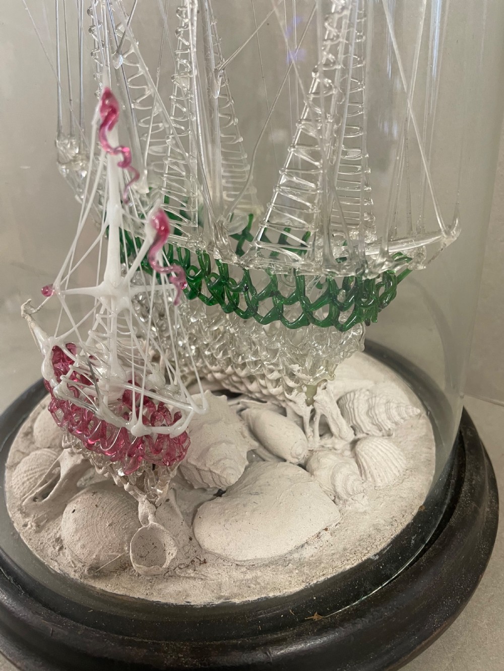 A detailed model of a sailing ship made from spun glass, enclosed inside a glass display dome on a dark wooden base. View III