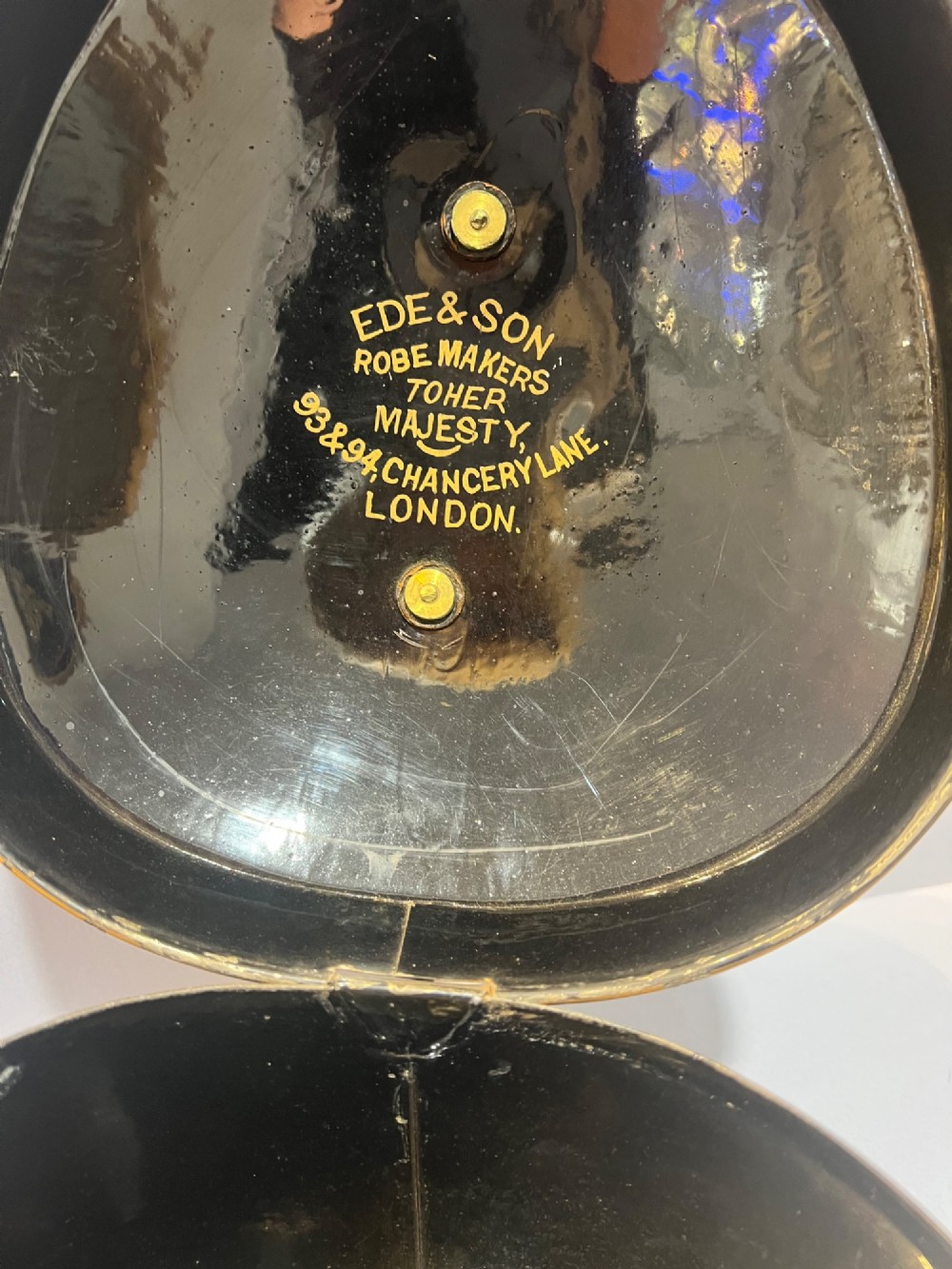 An antique horsehair barrister wig displayed on an internal wire stand next to a black painted metal tin case featuring gold lettering. View VI