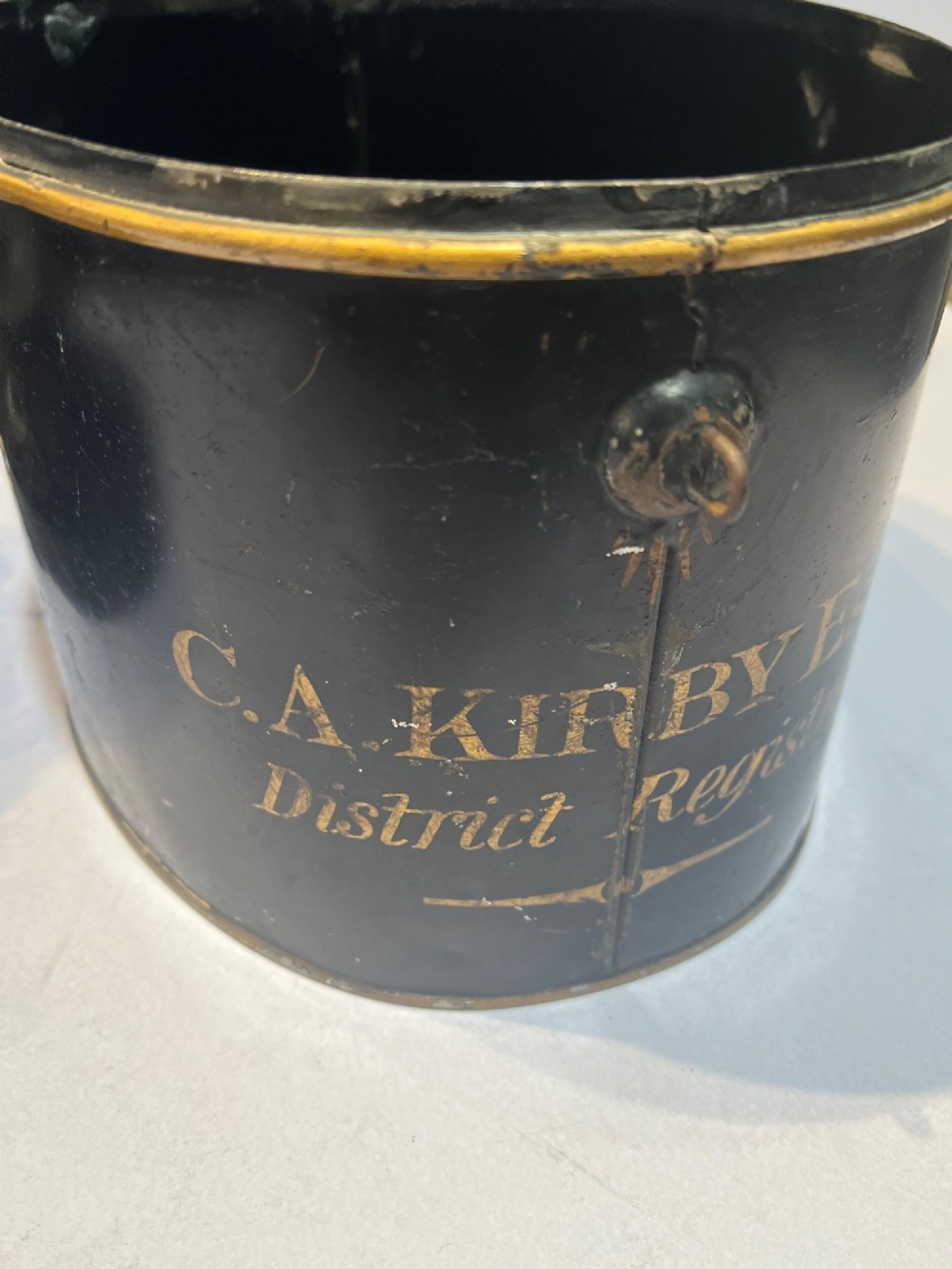 An antique horsehair barrister wig displayed on an internal wire stand next to a black painted metal tin case featuring gold lettering. View VIII