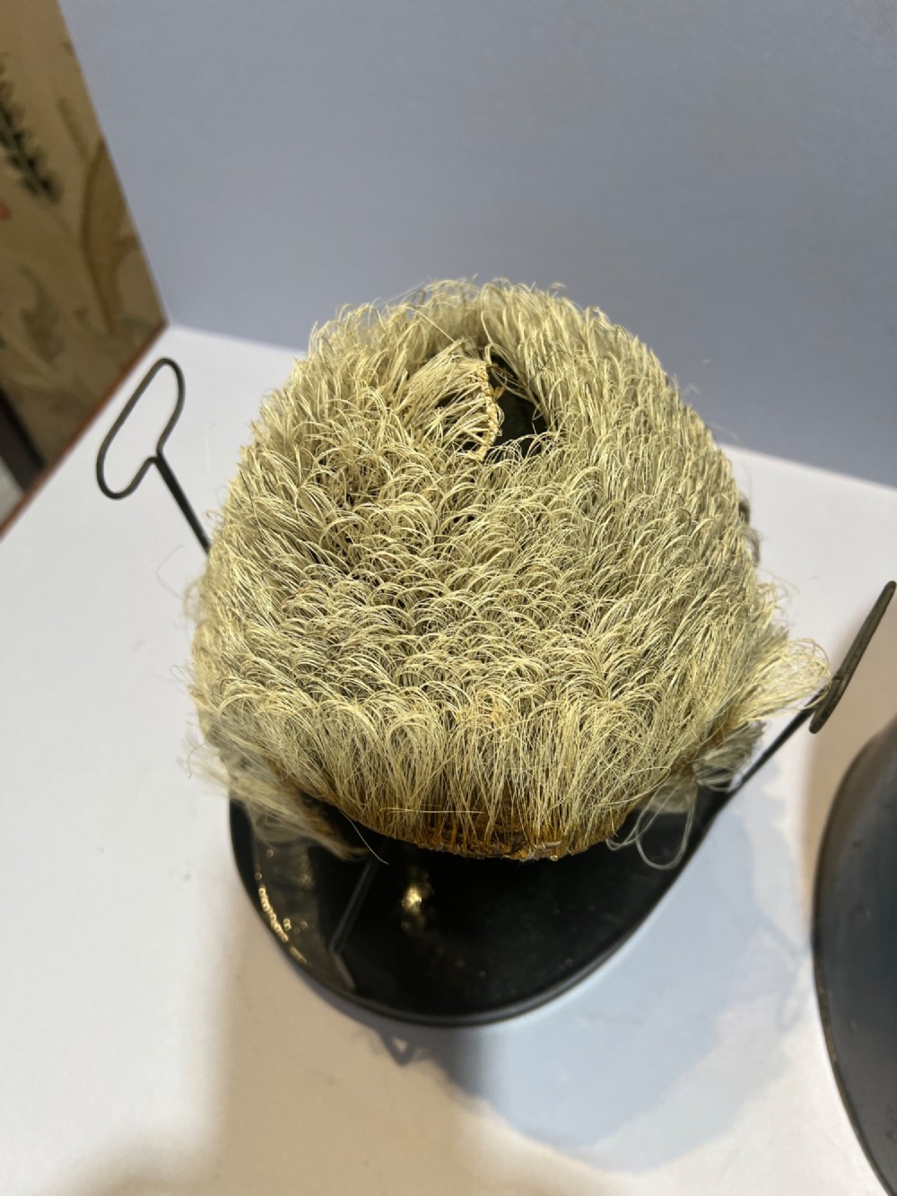 An antique horsehair barrister wig displayed on an internal wire stand next to a black painted metal tin case featuring gold lettering. View X