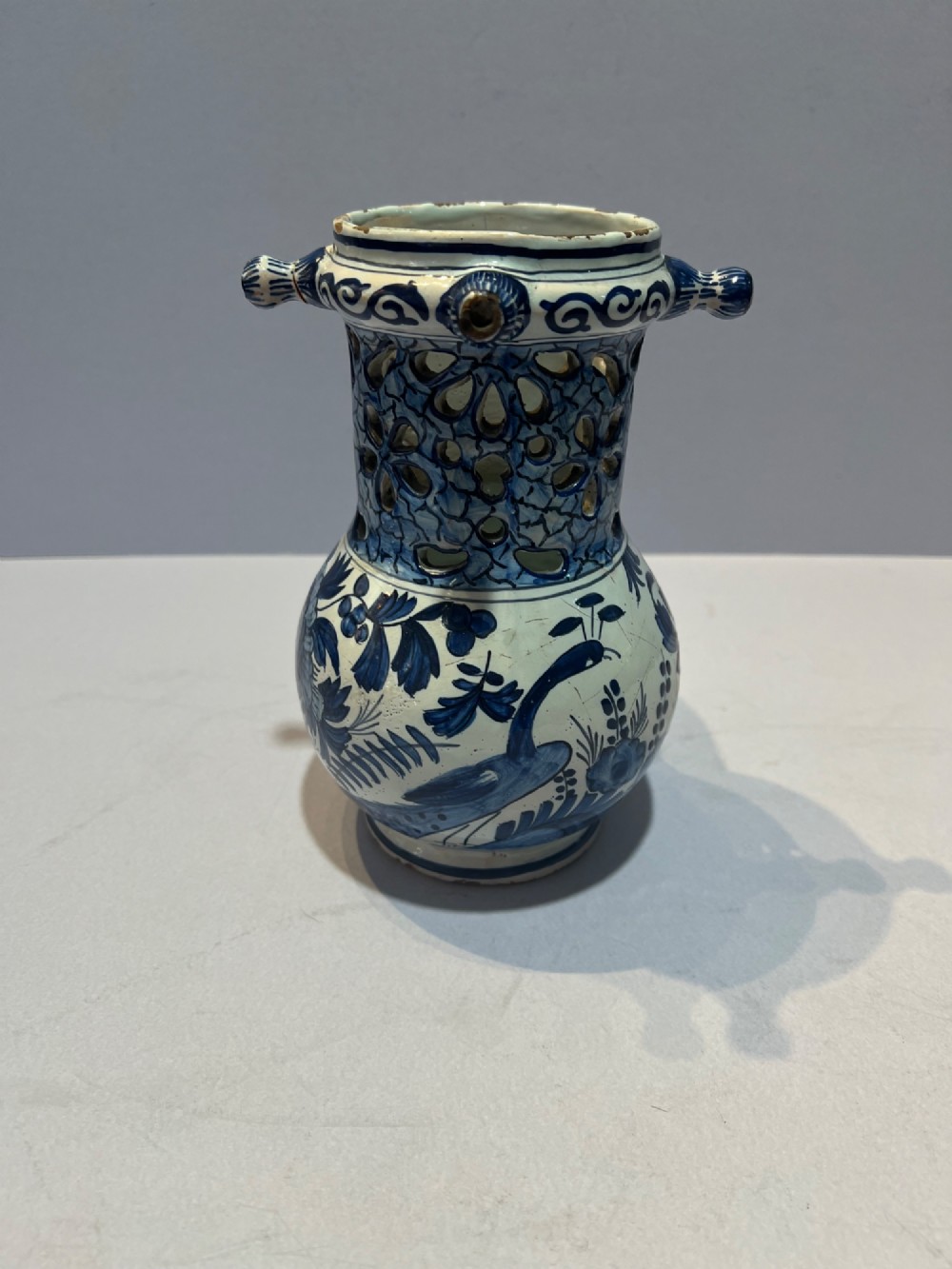 An 18th-century Dutch Delft tin-glazed earthenware puzzle jug featuring hand-painted blue floral motifs, a reticulated neck, and circular spouts along the upper rim. View III