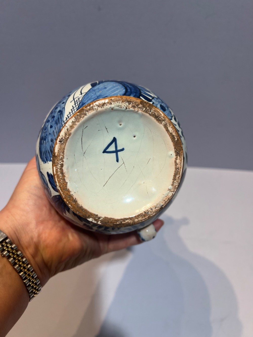 An 18th-century Dutch Delft tin-glazed earthenware puzzle jug featuring hand-painted blue floral motifs, a reticulated neck, and circular spouts along the upper rim. View VI