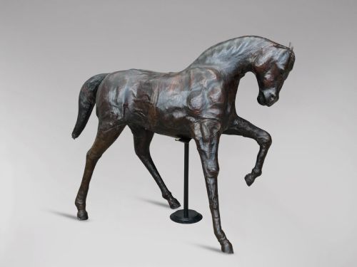 fig 1. A dark brown hand-stitched leather model of a horse in a trotting pose with one front leg raised.