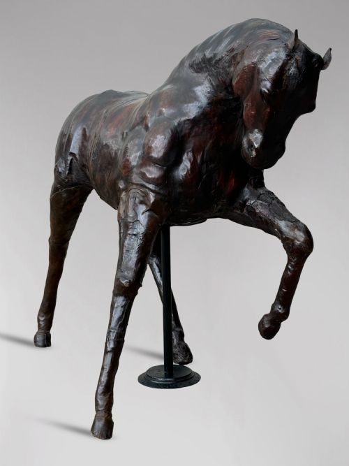 fig 2. A dark brown hand-stitched leather model of a horse in a trotting pose with one front leg raised.