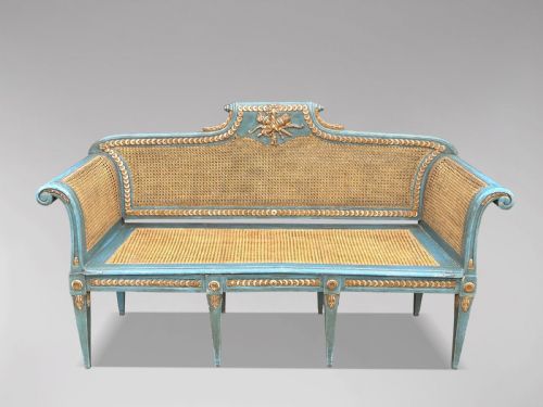 fig 1. A late 19th-century Louis XVI style settee featuring blue painted trim with gold leaf details, woven cane seat and back panels, and six fluted legs.