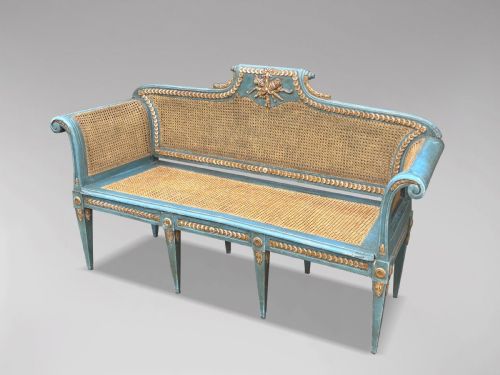 fig 2. A late 19th-century Louis XVI style settee featuring blue painted trim with gold leaf details, woven cane seat and back panels, and six fluted legs.