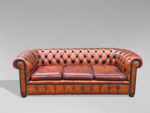fig 1. A three-seater brown leather Chesterfield sofa featuring deep button-tufted upholstery, rolled arms, brass studding, and three removable seat cushions.