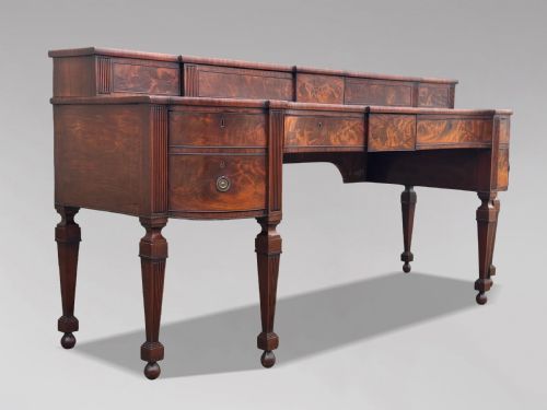 fig 1. An 18th-century George III flame mahogany sideboard featuring a raised stage back, oval wood inlays, fluted side columns, and six turned reeded legs.