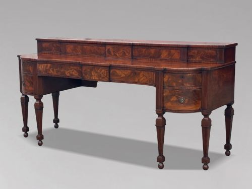 fig 2. An 18th-century George III flame mahogany sideboard featuring a raised stage back, oval wood inlays, fluted side columns, and six turned reeded legs.