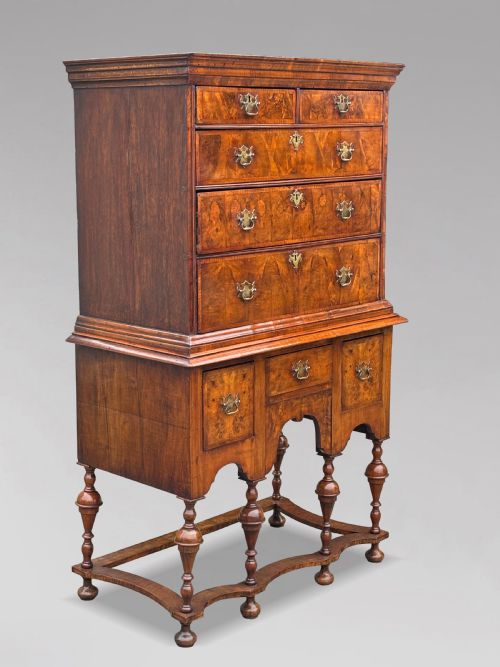 fig 1. An 18th-century Queen Anne walnut chest on stand featuring figured veneers, brass drop handles, a shaped lower apron, and turned legs joined by stretchers.