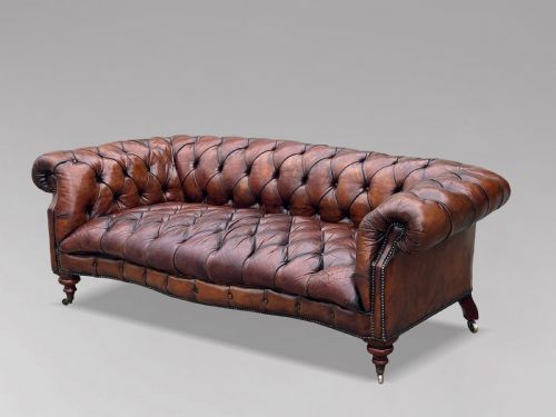 fig 1. A late 19th-century Victorian brown leather Chesterfield sofa featuring deep buttoned upholstery, rolled arms, close studding, and turned legs with brass castors.