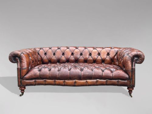 fig 2. A late 19th-century Victorian brown leather Chesterfield sofa featuring deep buttoned upholstery, rolled arms, close studding, and turned legs with brass castors.