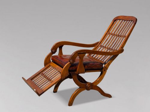 fig 2. A pair of 19th-century Victorian walnut reclining armchairs featuring slatted backrests, extendable footrests, curved X-frame bases, and brown leather seat cushions.