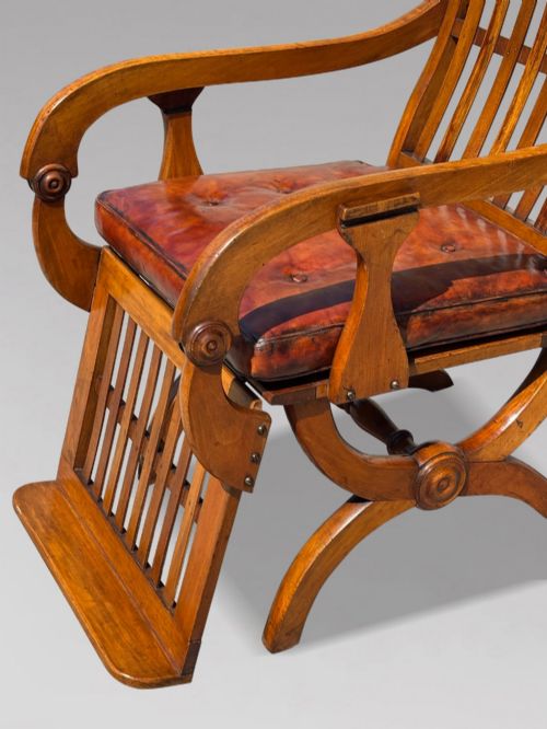 fig 4. A pair of 19th-century Victorian walnut reclining armchairs featuring slatted backrests, extendable footrests, curved X-frame bases, and brown leather seat cushions.