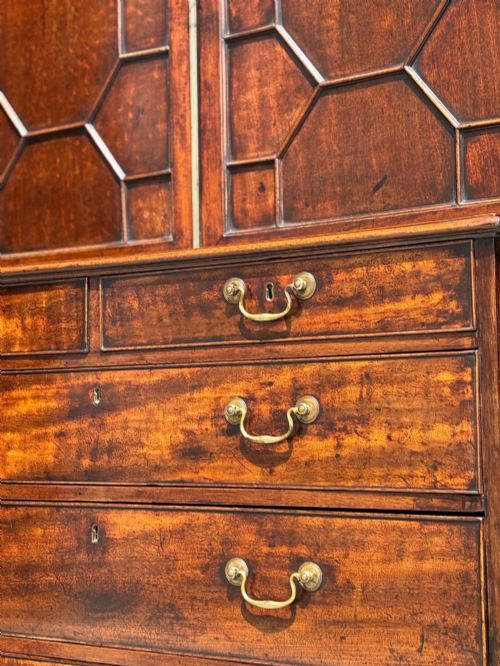 fig 4. An 18th-century George III mahogany bookcase on chest featuring a broken pediment, carved frieze, geometric astragal glazed doors, and four lower drawers with brass handles.