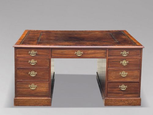 fig 1. An 18th-century George III mahogany partners desk featuring an inset leather writing surface, brass swan-neck handles, and twin pedestals with stacked drawers.