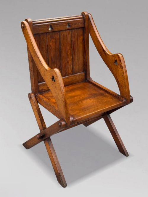 fig 2. A pair of Victorian pitch pine Glastonbury armchairs featuring sloped armrests, X-frame bases, and pierced trefoil motifs on the back panels.