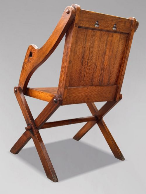 fig 3. A pair of Victorian pitch pine Glastonbury armchairs featuring sloped armrests, X-frame bases, and pierced trefoil motifs on the back panels.