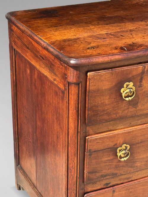 fig 1. A 17th-century French Provincial walnut commode featuring three long drawers decorated with brass drop handles and central escutcheons.