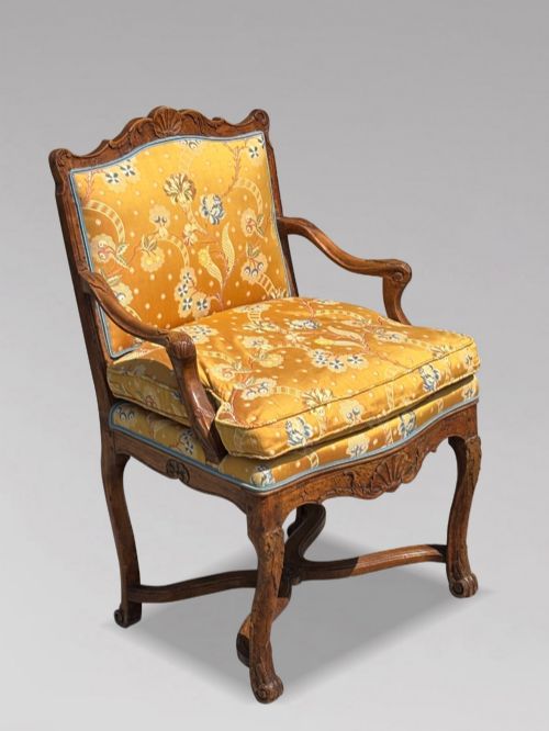 fig 3. An 18th-century French carved walnut armchair with cabriole legs, an X-form stretcher, and yellow floral upholstered cushions finished with blue trim.