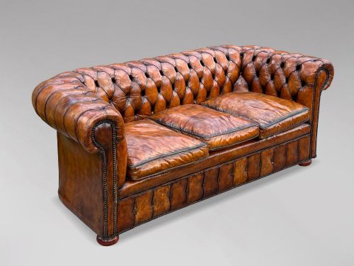 fig 1. A Victorian three-seater Chesterfield sofa with brown deep-buttoned leather, three seat cushions, brass stud trim, and turned feet.