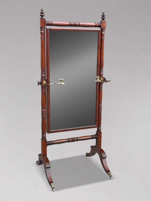 fig 1. An early 19th-century Regency mahogany cheval mirror featuring turned uprights, brass candle sconces, finials, and splayed legs on brass castors.